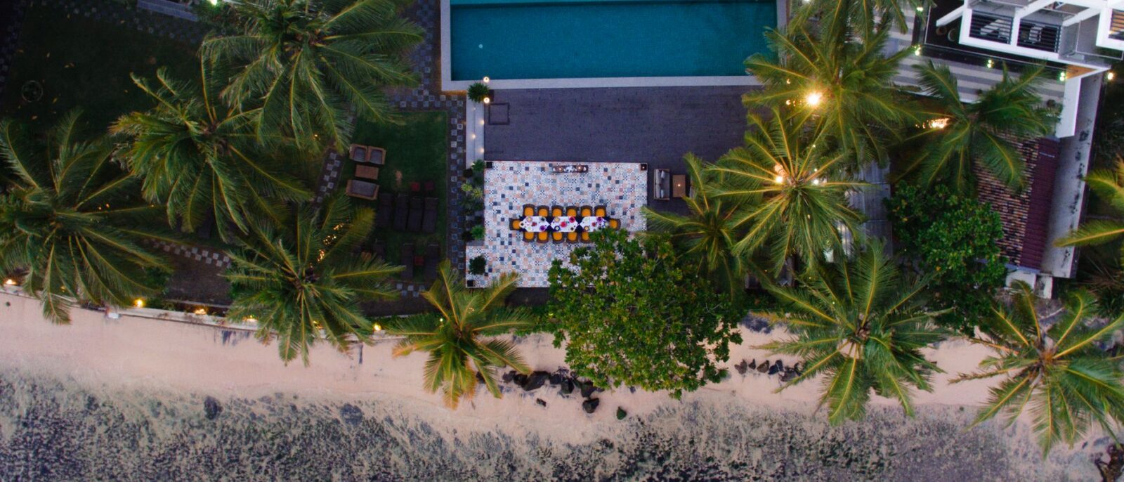 Vista aérea deslumbrante de um resort tropical com piscina à beira-mar cercada por palmeiras